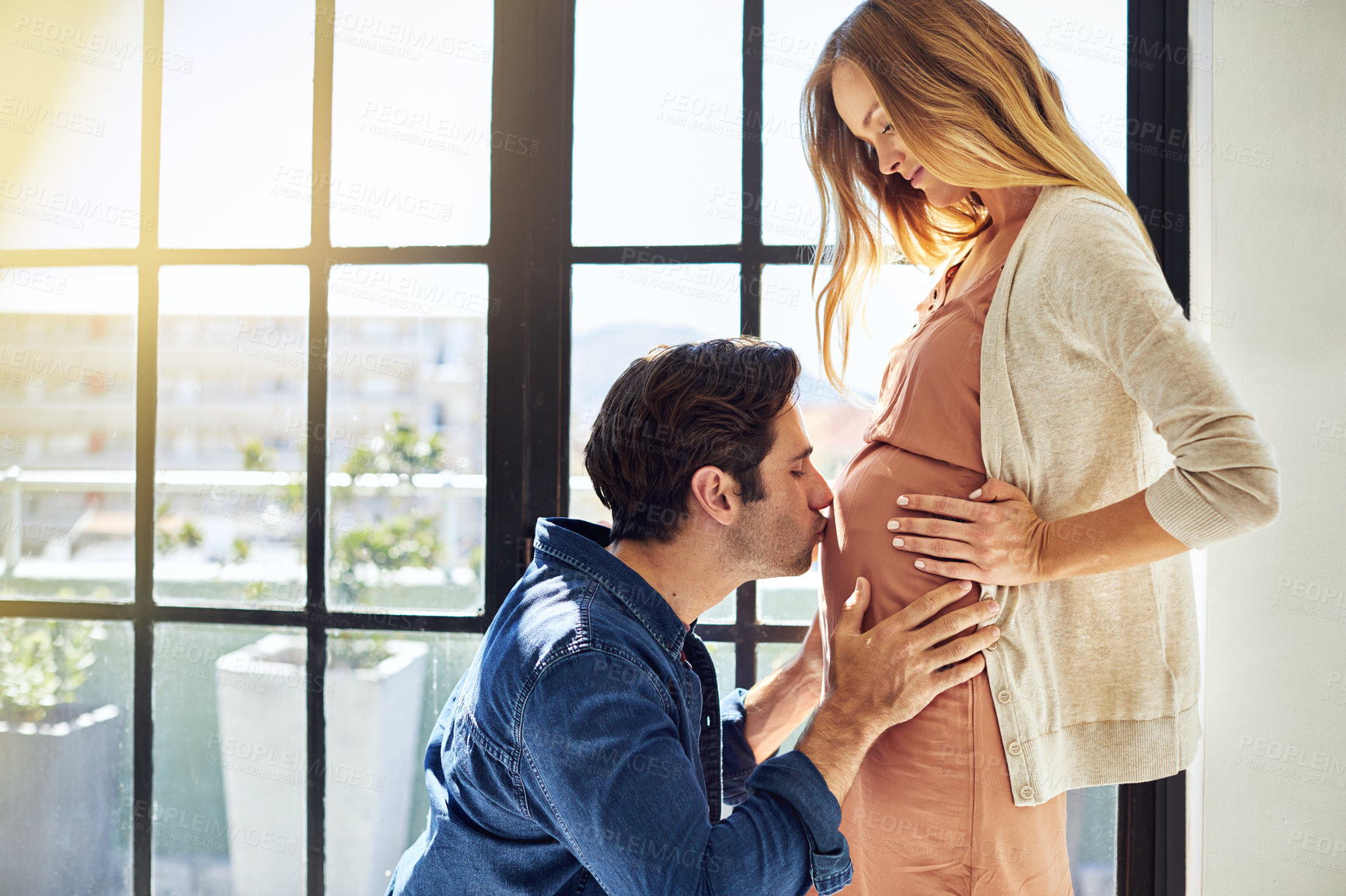 Buy stock photo Shot of a young man kissing his pregnant wife's tummy at home
