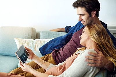 Buy stock photo Shot of a young man and his pregnant wife looking at a sonogram on a digital tablet on the sofa