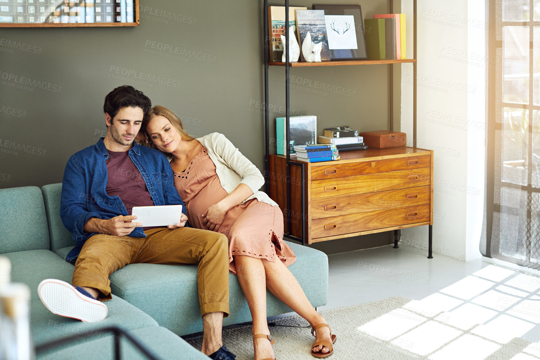 Buy stock photo Shot of a young man and his pregnant wife using a digital tablet together on the sofa
