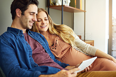 Buy stock photo Shot of a young man and his pregnant wife using a digital tablet together on the sofa