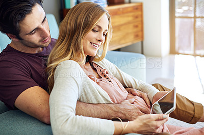 Buy stock photo Shot of a young man and his pregnant wife using a digital tablet together on the sofa