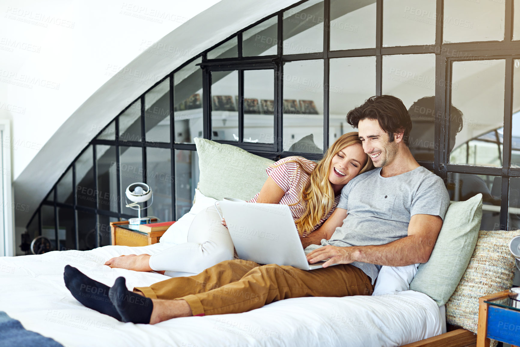 Buy stock photo Shot of a young couple using a laptop together while relaxing on the bed at home