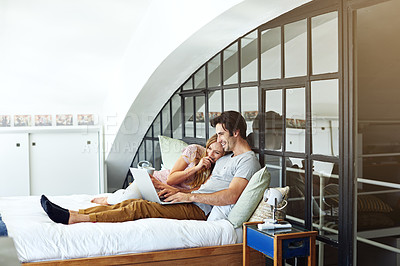 Buy stock photo Shot of a young couple using a laptop together while relaxing on the bed at home