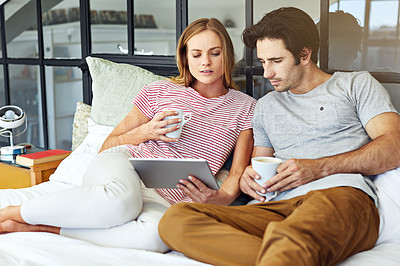 Buy stock photo Shot of a young couple using a digital tablet together while relaxing on the sofa at home