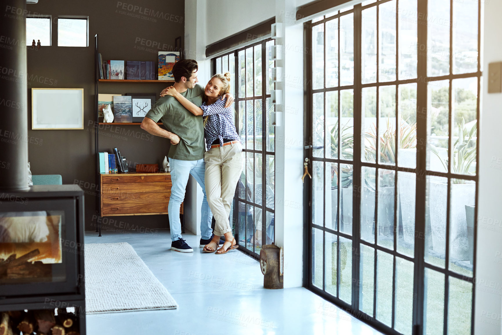 Buy stock photo Couple, hug and happy by window in home for bonding, quality time and together for peace. Man, woman and smile with calm for commitment, comfortable and trust by glass door with relationship wellness