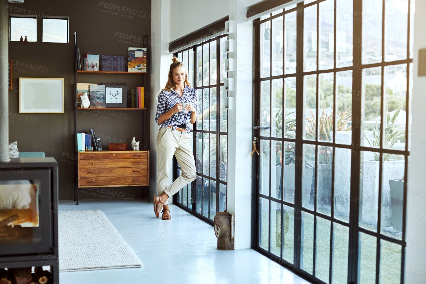 Buy stock photo Full length shot of an attractive young woman enjoying a coffee while standing by a glass door at home