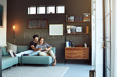 Buy stock photo Shot of a young couple using a digital tablet together while relaxing on the sofa at home