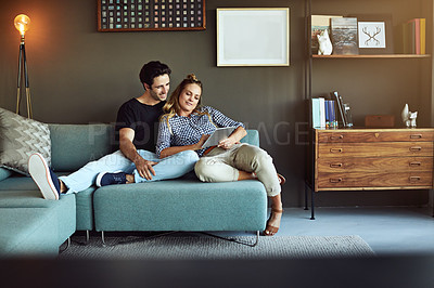 Buy stock photo Shot of a young couple using a digital tablet together while relaxing on the sofa at home