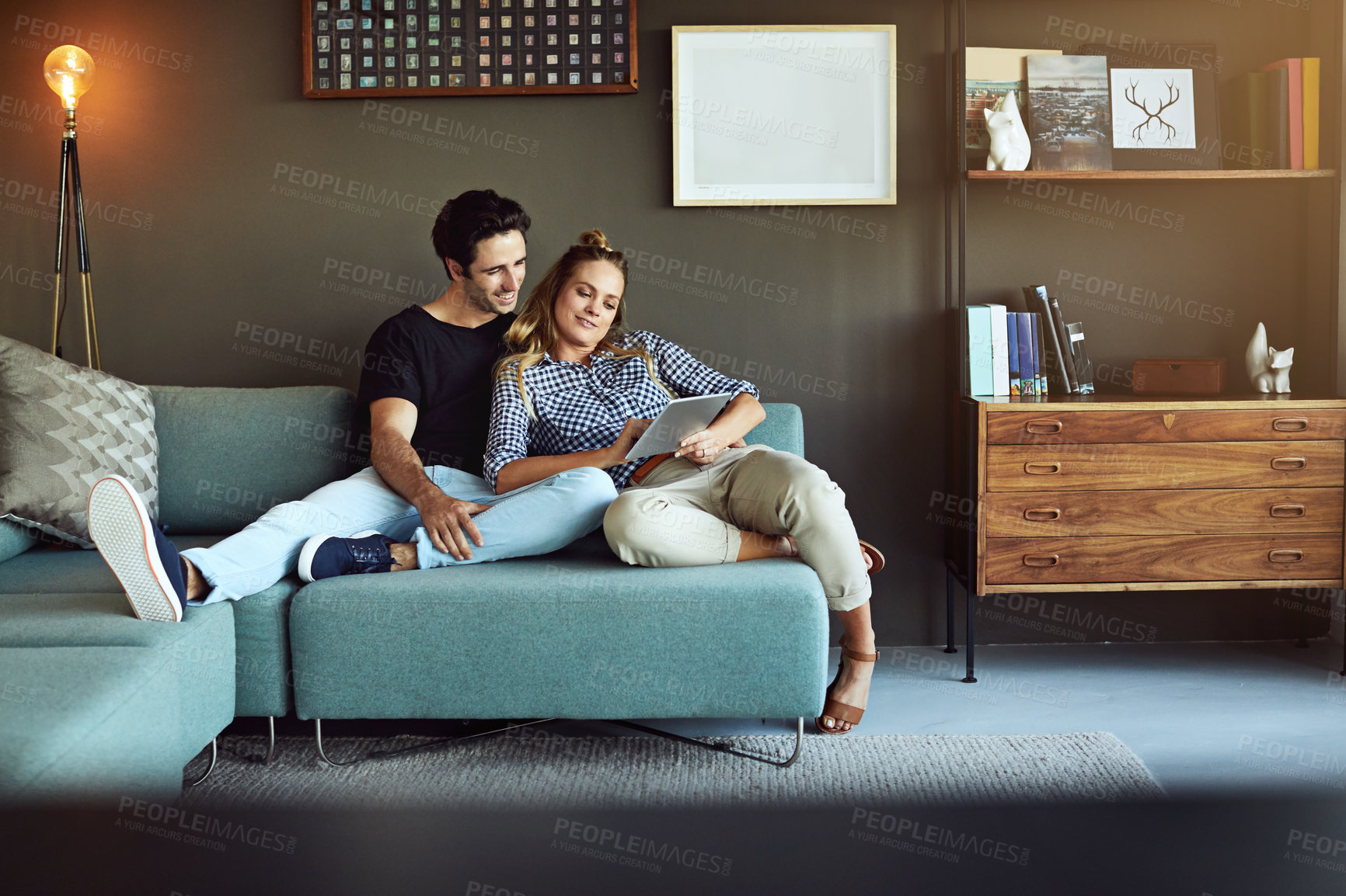 Buy stock photo Shot of a young couple using a digital tablet together while relaxing on the sofa at home