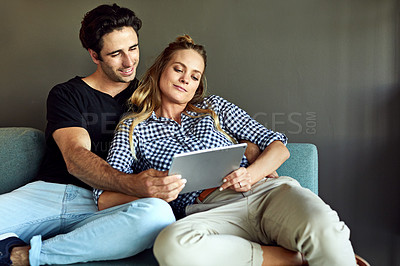 Buy stock photo Shot of a young couple using a digital tablet together while relaxing on the sofa at home