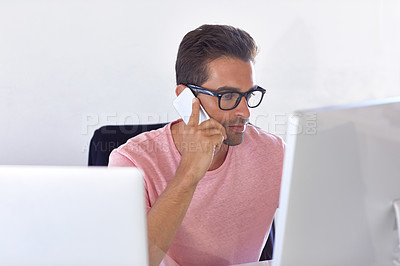 Buy stock photo Shot of a young businessman talking on his phone while sitting at his desk