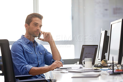 Buy stock photo Shot of a young businessman talking on his phone while sitting at his desk