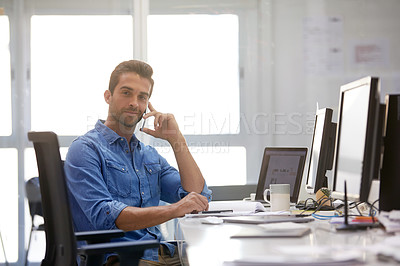 Buy stock photo Shot of a young businessman talking on his phone while sitting at his desk