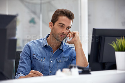 Buy stock photo Shot of a young businessman talking on his phone while sitting at his desk