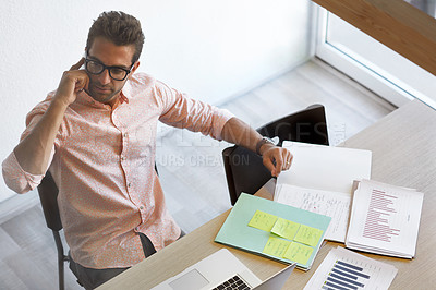 Buy stock photo Shot of a young businessman talking on his phone while sitting at his desk