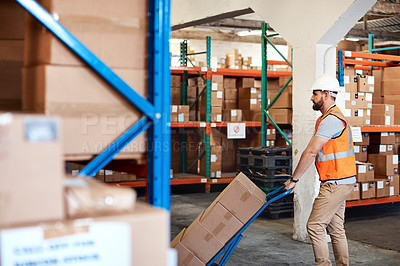 Buy stock photo Shot of a young man moving boxes on a trolley in a warehouse