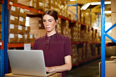 Buy stock photo Shot of a young woman using a laptop in a warehouse