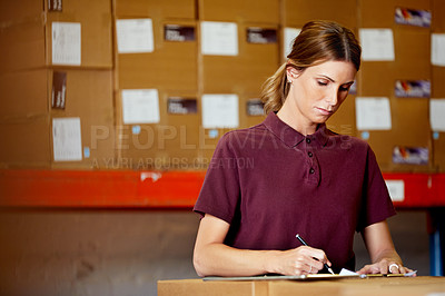 Buy stock photo Shot of a young woman writing notes while working in a warehouse