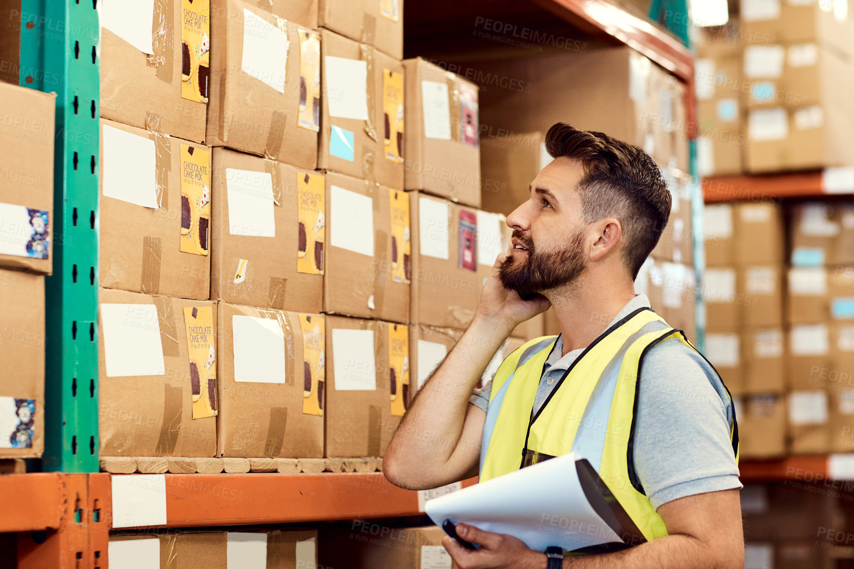 Buy stock photo Shot of a young man talking on a cellphone while working in a warehouse