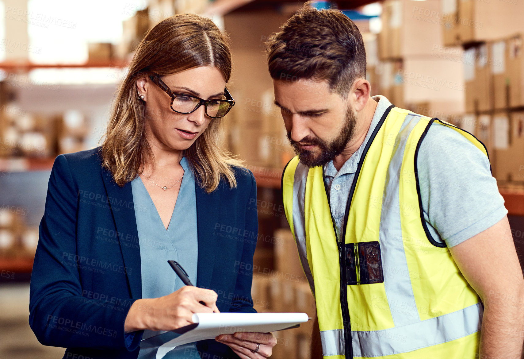 Buy stock photo Shot of a young man and woman going through notes on a clipboard in a warehouse