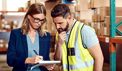 Buy stock photo Shot of a young man and woman going through notes on a clipboard in a warehouse