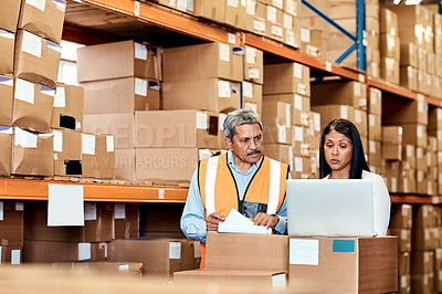 Buy stock photo Shot of a mature man and woman going through paperwork while using a laptop in a warehouse