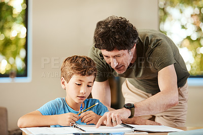 Buy stock photo Shot of a cute little boy doing homework with his father at home