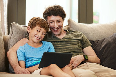 Buy stock photo Shot of a cute little boy using a digital tablet with his father at home