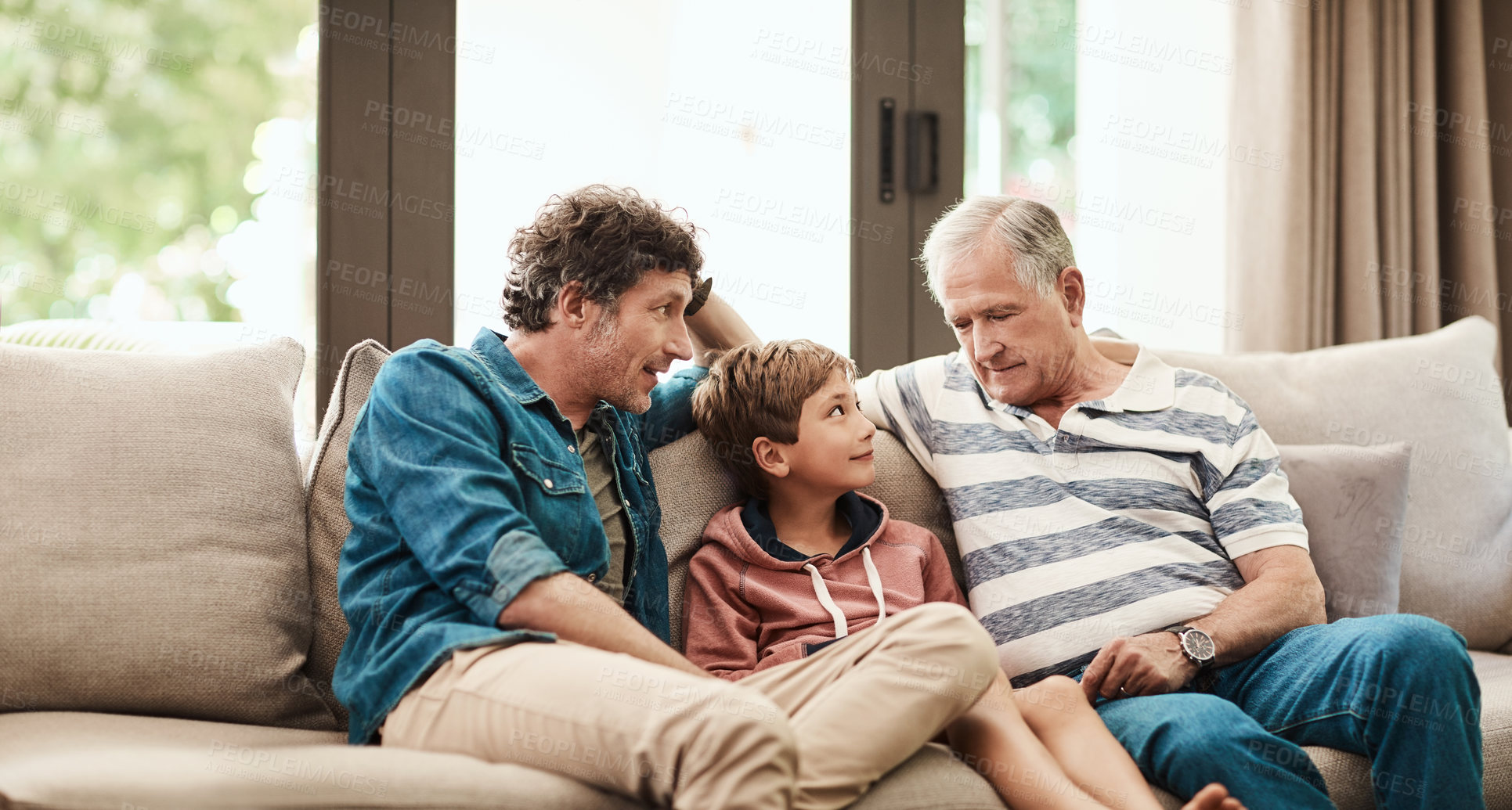 Buy stock photo Shot of an adorable little boy relaxing on the sofa with his father and grandfather at home