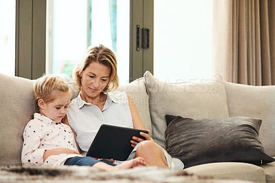 Buy stock photo Shot of a cute little girl using a digital tablet with her mother at home