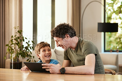 Buy stock photo Shot of a cute little boy using a digital tablet with his father at home