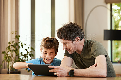Buy stock photo Shot of a cute little boy using a digital tablet with his father at home