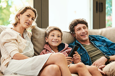 Buy stock photo Shot of an adorable young boy watching tv with his parents on the sofa at home