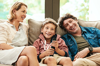 Buy stock photo Shot of an adorable young boy watching tv with his parents on the sofa at home
