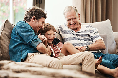 Buy stock photo Shot of an adorable little boy relaxing on the sofa with his father and grandfather at home