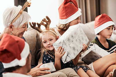 Buy stock photo Cropped shot of a cheerful little girl holding a present while being seated with her family during Christmas time