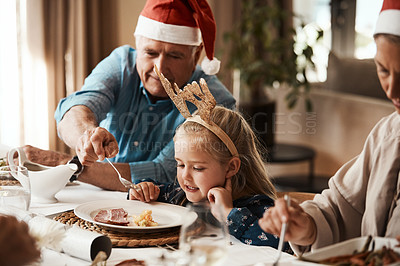 Buy stock photo Cropped shot of a cheerful elderly man dishing food into his granddaughter's plate at lunch during Christmas time