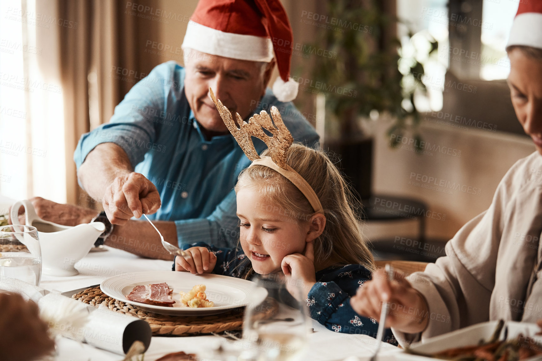 Buy stock photo Cropped shot of a cheerful elderly man dishing food into his granddaughter's plate at lunch during Christmas time