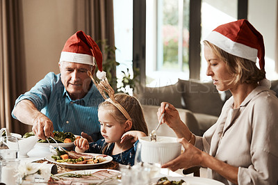 Buy stock photo Cropped shot of a cheerful elderly man dishing food into his granddaughter's plate at lunch during Christmas time