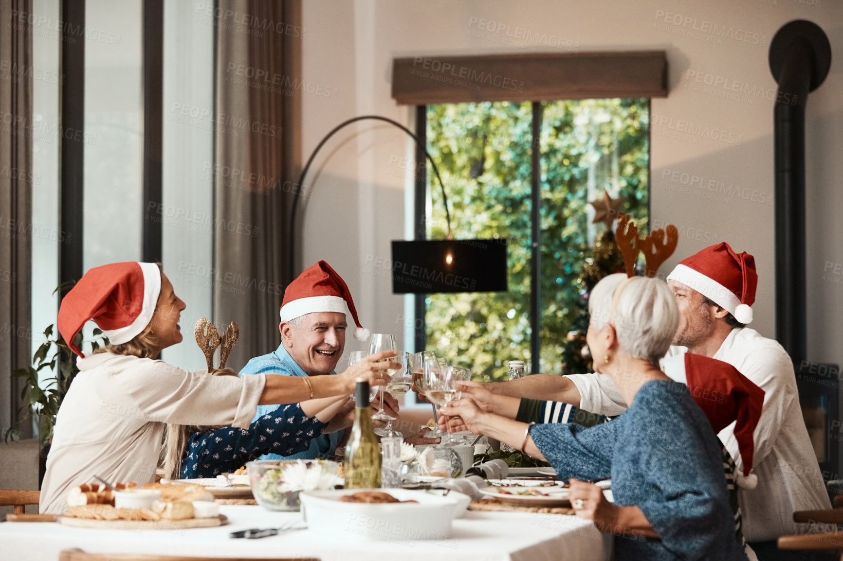 Buy stock photo Christmas, cheers and big family in home for celebration, annual tradition and generations at lunch. Happy parents, children and toast with drink for festive season, matching hats or feast at reunion