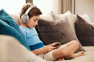Buy stock photo Shot of a cute little boy using a digital tablet with headphones on the sofa at home