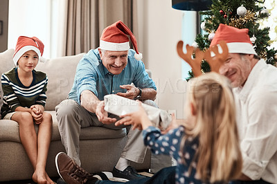 Buy stock photo Cropped shot of a cheerful elderly man giving his granddaughter a present while being seated with family during Christmas time