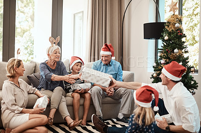 Buy stock photo Shot of a cheerful family opening presents together while being seated on a sofa during Christmas time