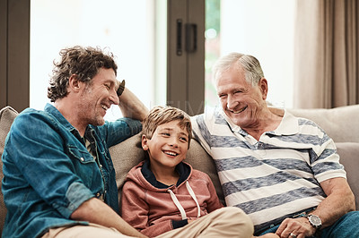 Buy stock photo Cropped shot of a cheerful little boy seated on a sofa with his father and grandfather during Christmas time