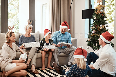 Buy stock photo Shot of a cheerful family opening presents together while being seated on a sofa during Christmas time