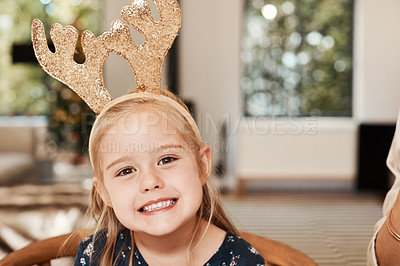 Buy stock photo Portrait of a cheerful little girl wearing reindeer antlers while being seated with family at a lunch table during Christmas time
