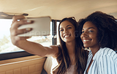 Buy stock photo Shot of two happy young friends taking selfies during a road trip