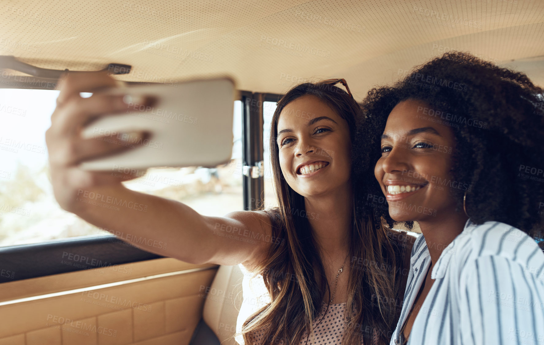 Buy stock photo Shot of two happy young friends taking selfies during a road trip