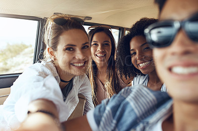 Buy stock photo Shot of a group of happy young friends taking selfies during a road trip