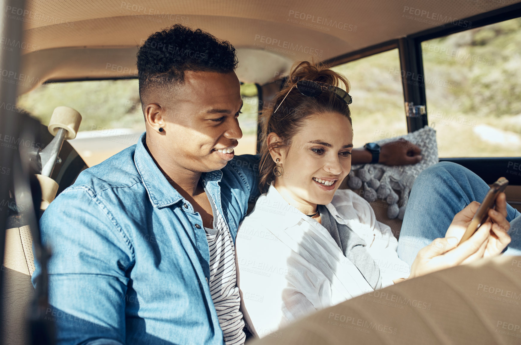 Buy stock photo Shot of a happy young couple using a smartphone on a road trip